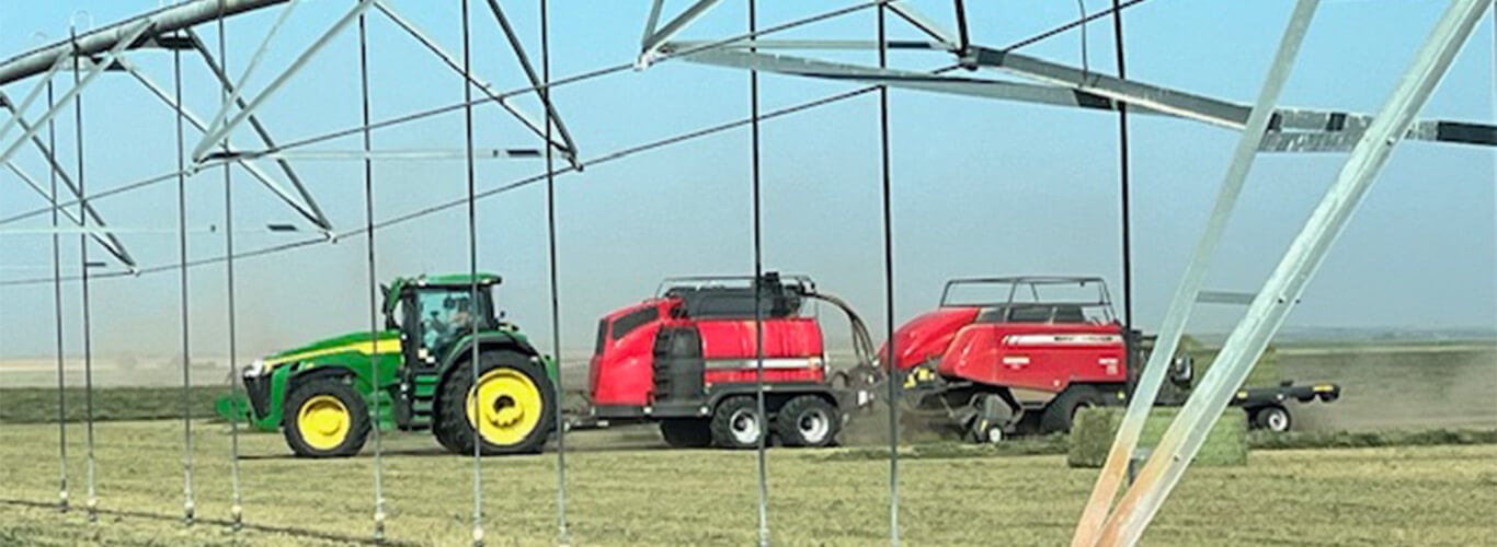 John Deere tractor pulling a steamer and square baler in front of pivot.