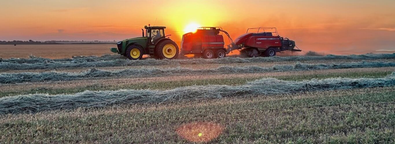 John Deere baling with a sunset in the background.